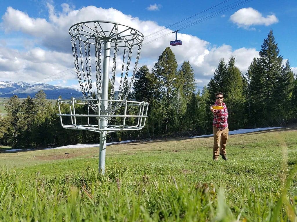 Man throwing a frisbee disc into a golf goal post in a field near Teton Village in Jackson Hole, Wyoming