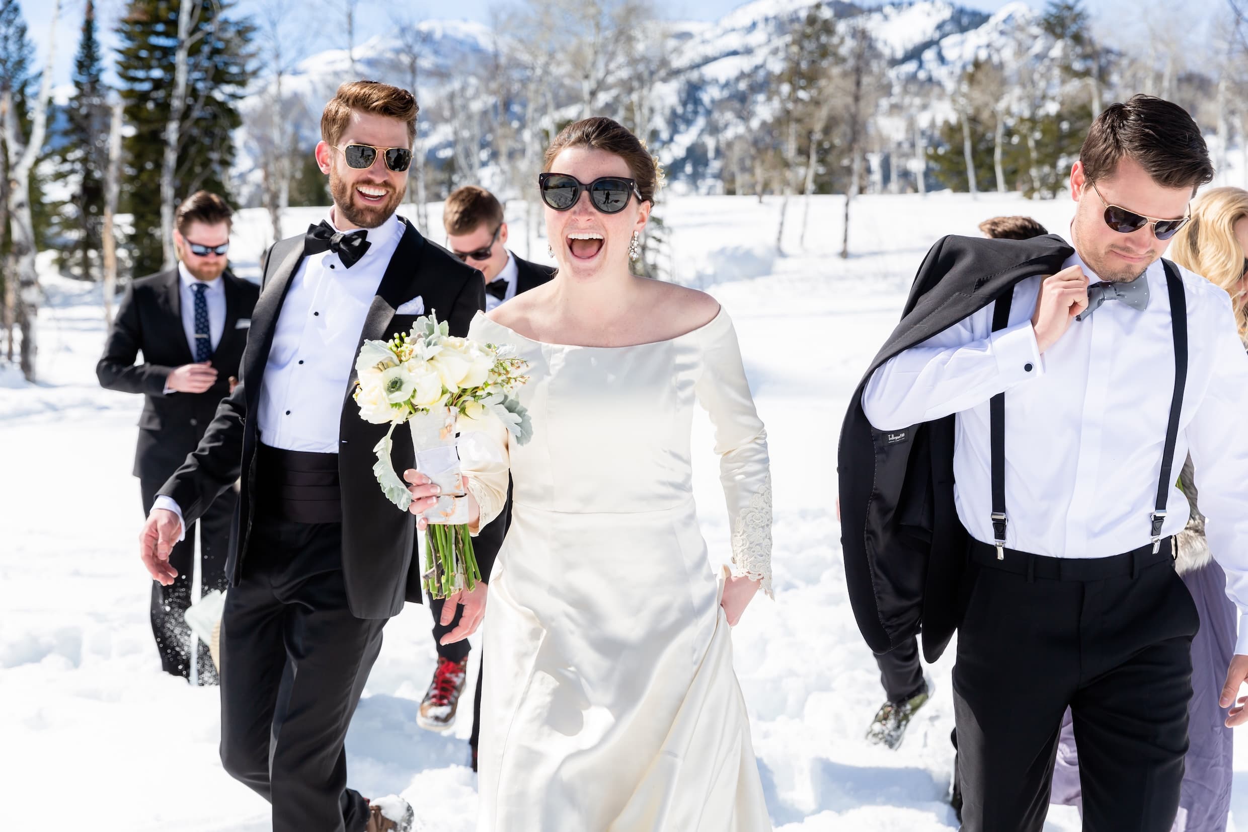 A groom and bride walking through the snow followed by the groomsmen at a Winter wedding in Jackson Hole, Wyoming.